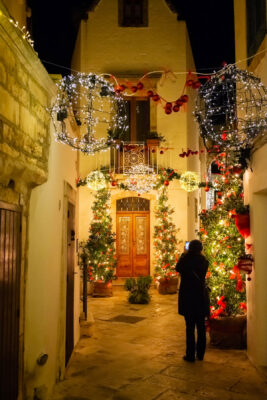 girl takes a picture of christmas decorated alley in locorotondo at night.